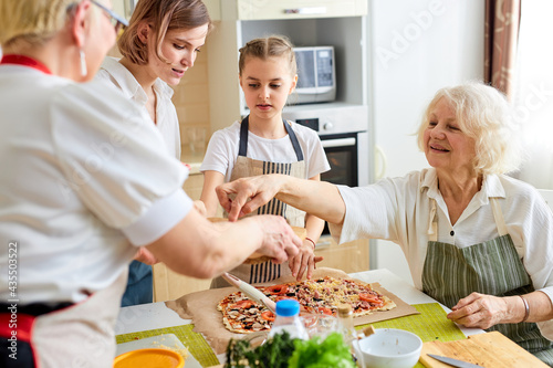 Family having fun making pizza together. grandwoman and children in the kitchen together, help each other, wearing apron. Concept of homemade food and little helpers.