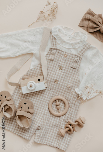 Flat lay Baby natural material accessories concept. Wooden toys, clothes and shoes on beige background. Bohemian baby fashion.