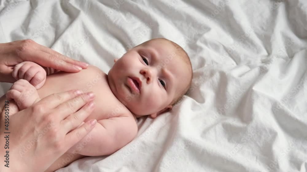 Mother massaging little baby. Newborn Baby skin care concept. Prevention of colic. Female hands doing massage to newborn. Slow motion. Nice caucasian infant baby lying at the back. Portrait. Close up. Mother massaging little baby. Newborn Baby skin care concept. Prevention of colic. Female hands doing massage to newborn. Slow motion. Nice caucasian infant baby lying at the back. Portrait. Close up.