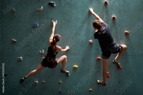 fitness, extreme sport, bouldering, people and healthy lifestyle concept - rear view on man and woman exercising at indoor climbing gym with safety equipment, training, in sportive outfit