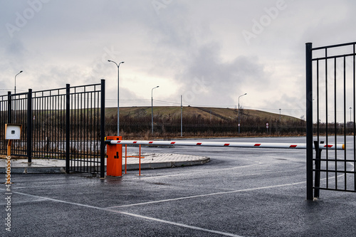 Automatic barrier of orange color with a white stripe and red warning stripes, for the entry of cars. Entrance to the car factory parking lot.