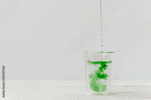 Drops of liquid chlorophyll falling down in a glass cup with water. Light white background with copy space photo