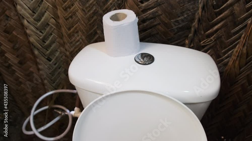 Toilet in an African grass hut, Zanzibar. Bathroom in a small thatched house on the ground. Inside the village house made of malocas, East Africa. White toilet bowl with toilet paper. Tanzania, Africa photo