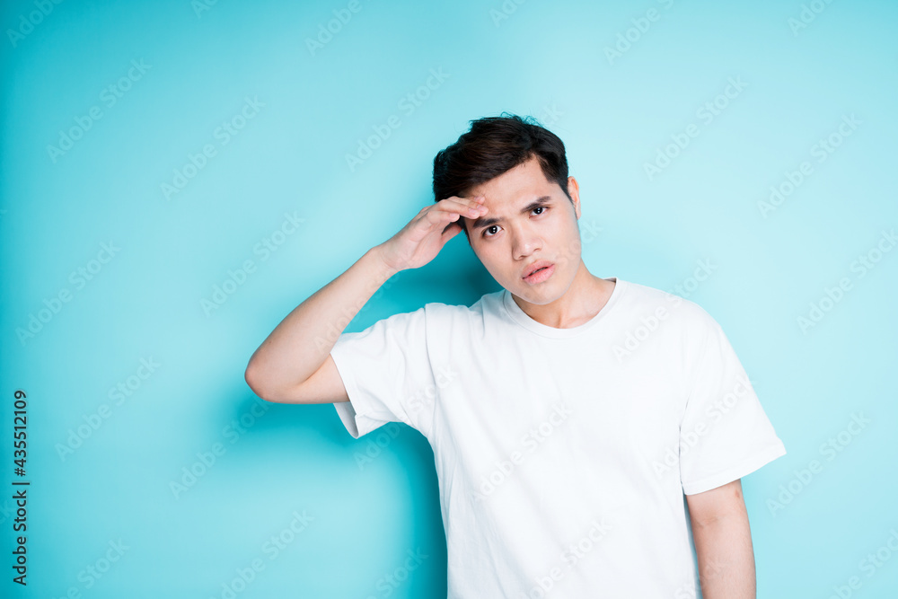 Young asian guy looking away with interest while holding his hand above his eyes while standing on a blue background Young asian guy looking away with interest while holding his hand above his eyes while standing on a blue background