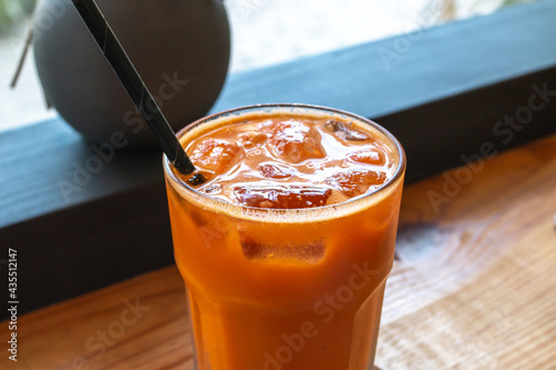 Soft-focus image of a tall glass of orange turmeric cold-pressed juice with a black compostable straw sitting on a wooden hard top bar table (window view) in a cafe in Holetown, Barbados.  photo