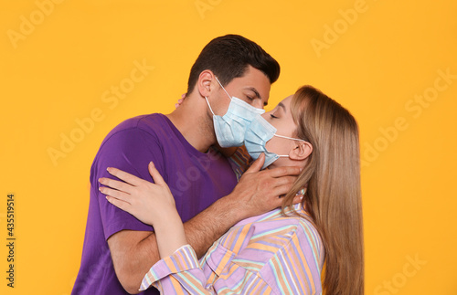 Couple in medical masks trying to kiss on yellow background photo