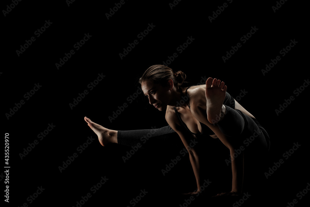 cute caucasian girl exercising yoga poses against dark backgroung. side lit silhouette.