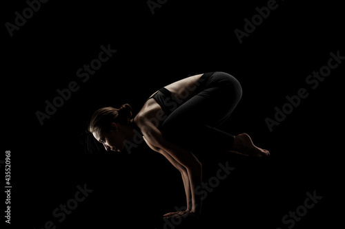cute caucasian girl exercising yoga poses against dark backgroung. side lit silhouette. © Nikola Spasenoski