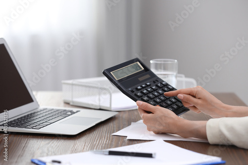 Woman using calculator at table indoors, closeup