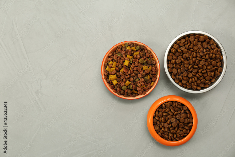 Dry food in pet bowls on grey background, flat lay. Space for text