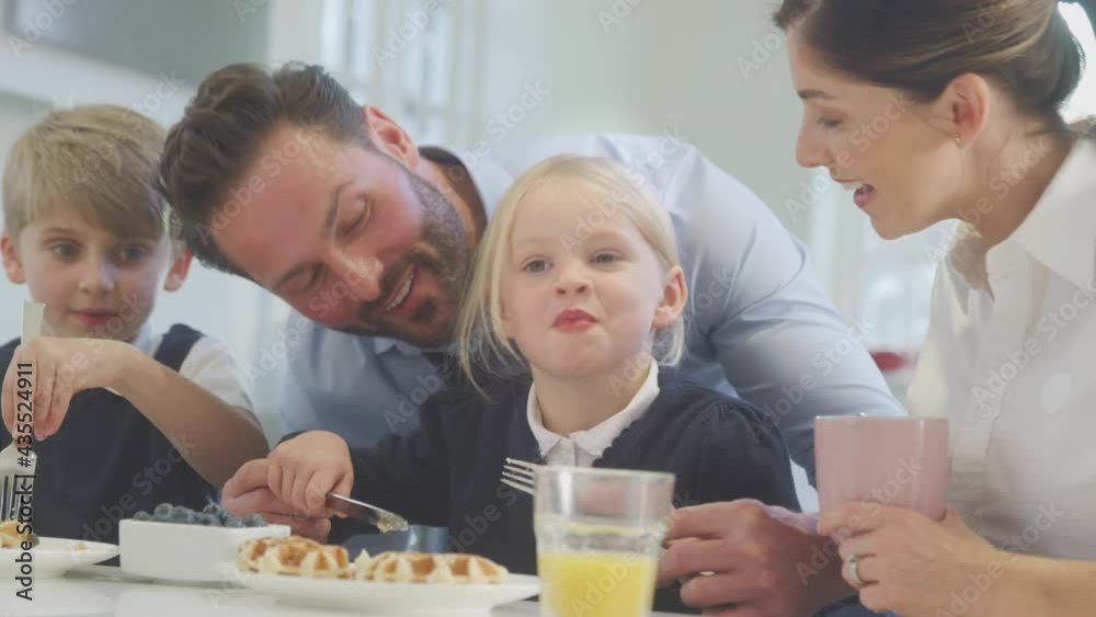 Close up of two children wearing school uniform in kitchen eating breakfast waffles as parents get ready for work - shot in slow motion Close up of two children wearing school uniform in kitchen eating breakfast waffles as parents get ready for work - shot in slow motion