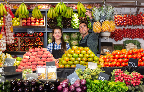 Portrait of young man and woman offering greens and vegetables on the market