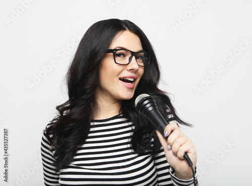 Young brunette woman in striped shirt and glasses holds microphone and prepares to sing in karaoke