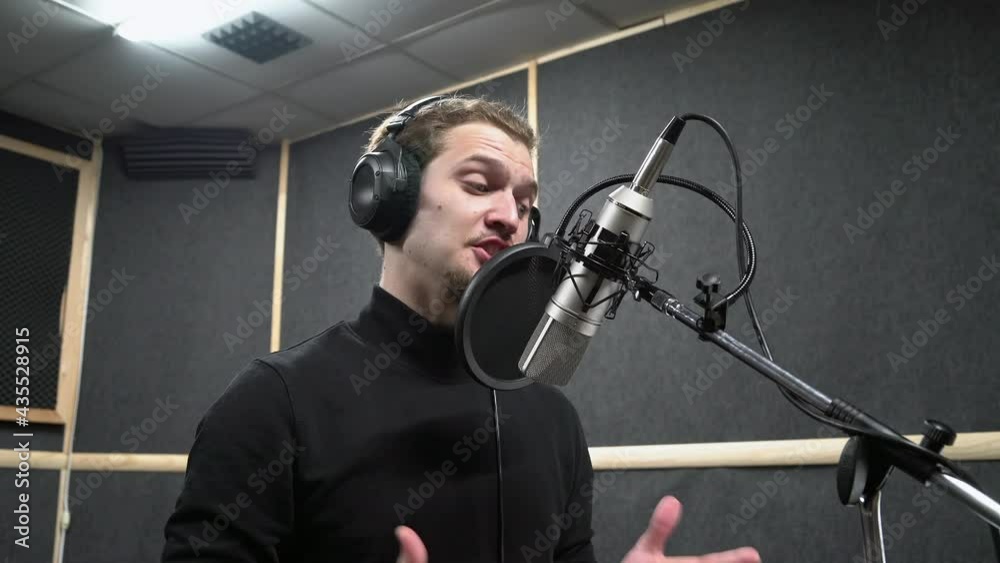 Voice actor in headphones on recording studio read a text near microphone to make a professional dubbing. Expressive scene of concentration near the microphone.
