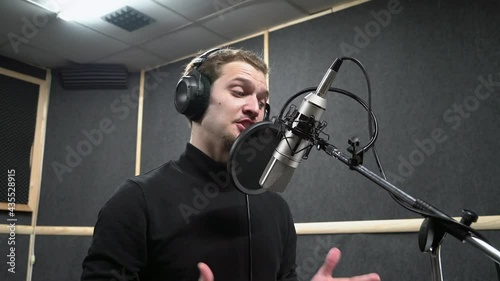 Voice actor in headphones on recording studio read a text near microphone to make a professional dubbing. Expressive scene of concentration near the microphone.