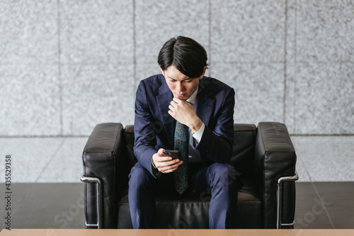 スマートフォンを注視する若い男性・オフィスに座る男性