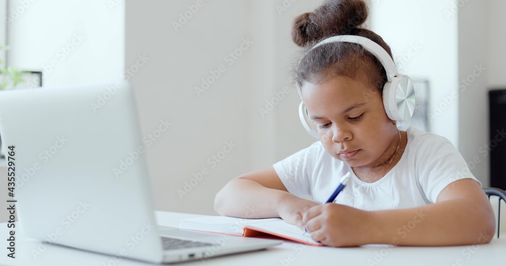 Afro american kid girl school pupil wearing headphones studying online from home watching web class lesson or listening tutor by video call elearning on pandemic isolation. Children remote education. Afro american kid girl school pupil wearing headphones studying online from home watching web class lesson or listening tutor by video call elearning on pandemic isolation. Children remote education.