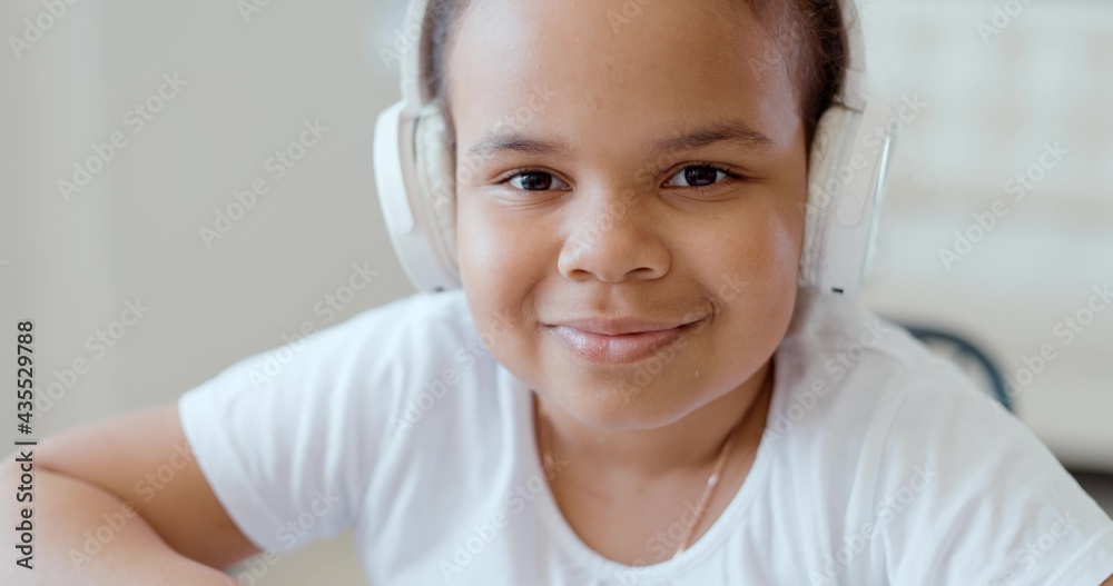 Afro american kid girl school pupil wearing headphones studying online from home watching web class lesson or listening tutor by video call elearning on pandemic isolation. Children remote education. Afro american kid girl school pupil wearing headphones studying online from home watching web class lesson or listening tutor by video call elearning on pandemic isolation. Children remote education.
