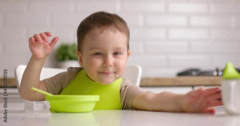 Small cute smile baby boy sitting at a table and plays with green dishes. Concept Happy Childhood Small cute smile baby boy sitting at a table and plays with green dishes. Concept Happy Childhood