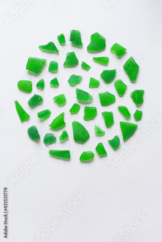 Round composition of various green assorted polished pieces of glass on a white background. Minimalistic natural background for invitation or greeting card with copy space.