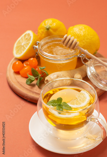 Ginger tea with mint and lemon. Healthy and hot drink. Liquid honey in honey-jar. Crystal cup on bright background. Selective focus.