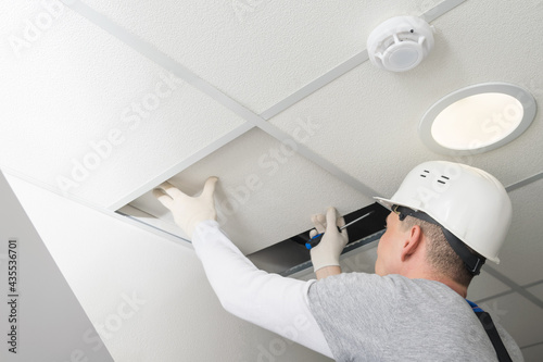 a worker in a helmet dismantles the suspended ceiling to test the lighting