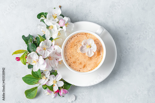 A cup of cappuccino and flowers on a gray background.