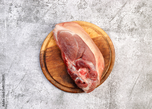 Raw pork shoulder on the skin with bone on a round wooden cutting board on a dark grey background. Top view, flat lay