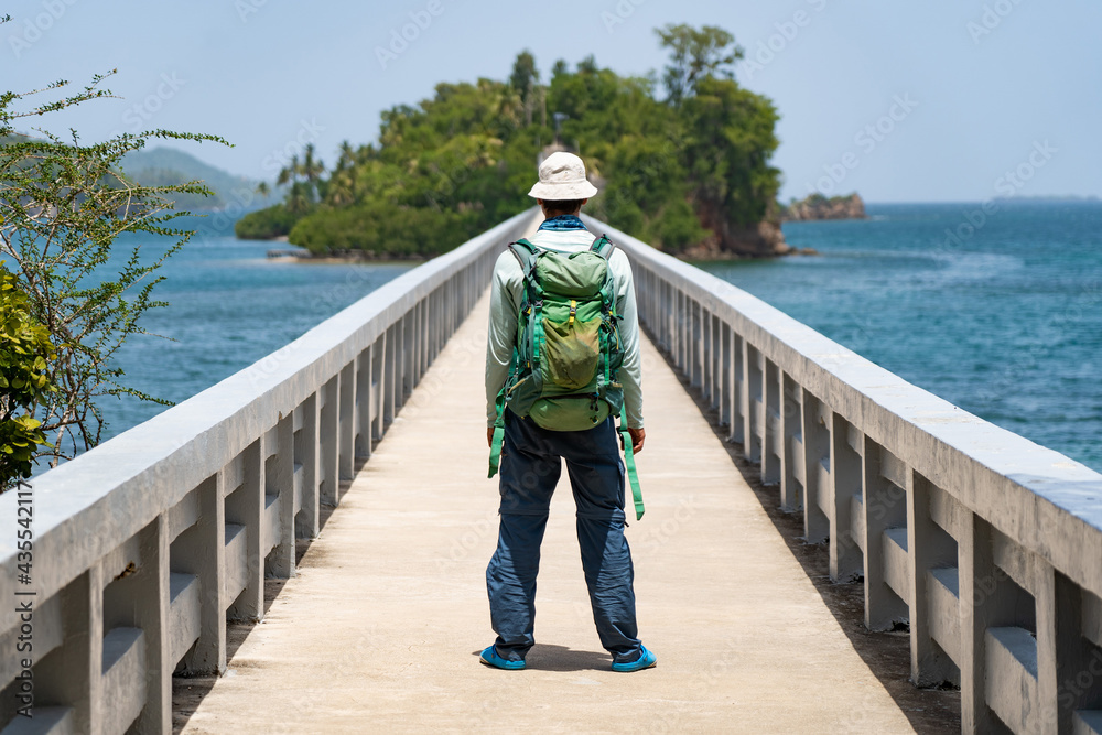Solo hiker with backpack on bridge which leads to island. Travel and adventure concept 
