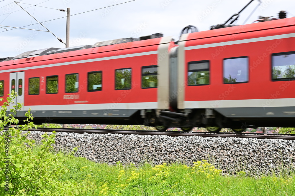 Vorbeifahrender roter Zug der deutschen Bahn mit Bewegungsunschärfe auf einer Bahntrasse durch grüne Landschaft