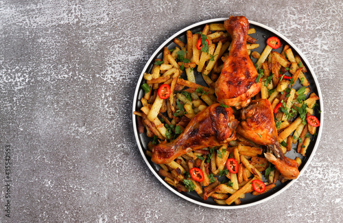 Chicken drumsticks with potatoes and hot peppers on a round plate on a dark background. Top view, flat lay