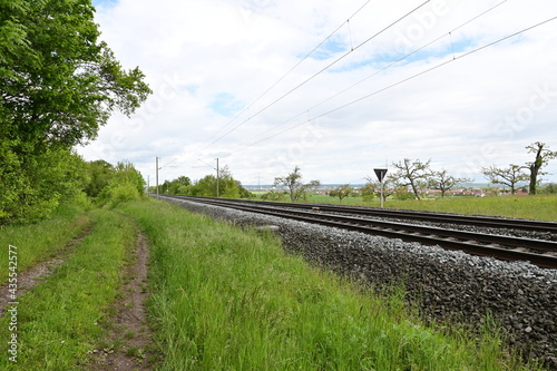 Fototapeta Naklejka Na Ścianę i Meble -  Railway line with 2 railway tracks and rails next to a dirt road near Bergrheinfeld, Schweinfurt, Bavaria, Germany