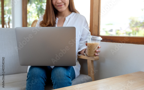 Closeup image of a beautiful young woman using and working on laptop computer while drinking coffee in cafe
