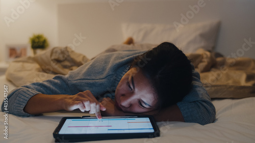 Freelance Asia women casual wear using laptop hard work on bed in bedroom at house night. Working from home, remotely work, self isolation, social distancing, quarantine for coronavirus prevention.