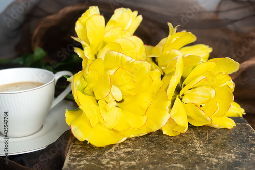 Still life. Yellow and orange tulips, cup of coffee and old book. Concept of congratulation