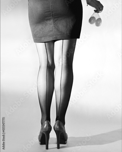 Women's legs in high-heeled shoes and in stockings with arrows. A girl in a dark miniskirt. Two chicken eggs in a bag in hand. 