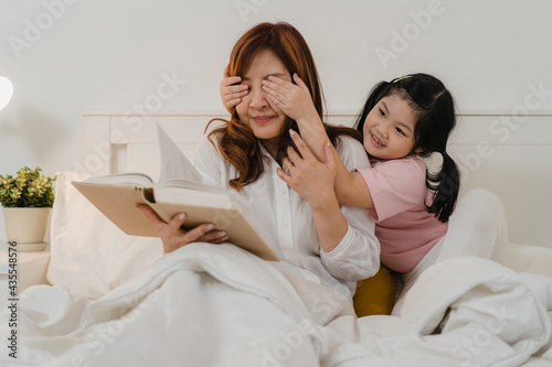Asian grandmother relax at home. Senior Chinese, grandma happy relax with young granddaughter girl enjoy close her eyes surprise playing together lying on bed in bedroom at home at night concept.