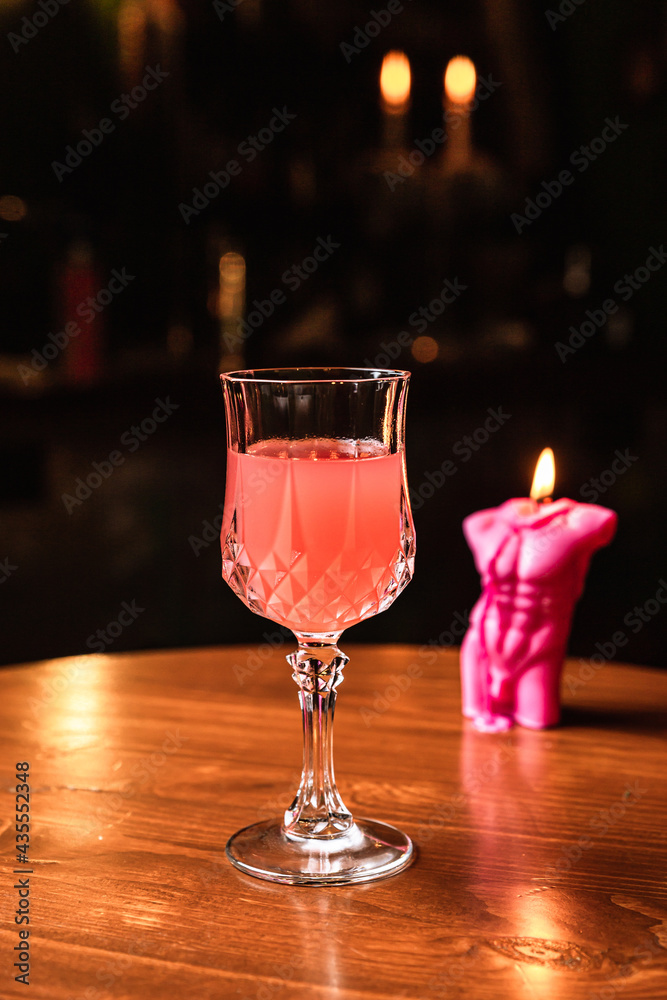 A pink cocktail in a beautiful crystal glass, a candle, on a wooden table, at the bar.