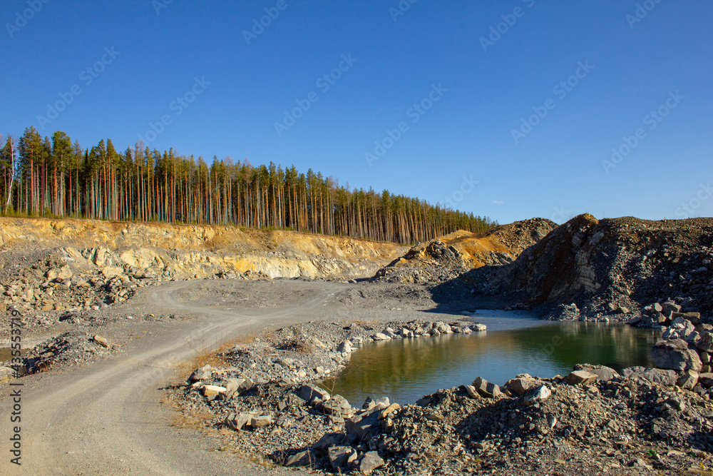 The beauty of a huge career in the Urals. Pine trees grow on quarries of a rocky quarry, mine workings, water at the bottom. Reddish rocks