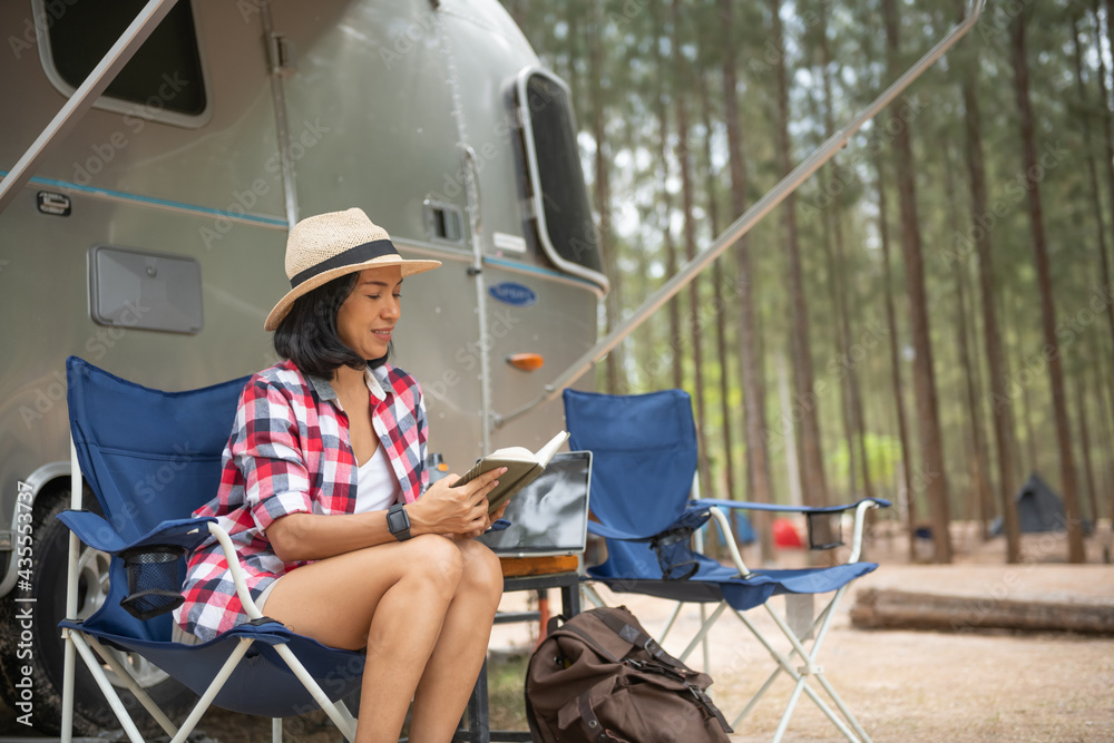 Woman looking at laptop near the camping. caravan car vacation. family vacation travel, holiday trip in motorhome. woman reading a book inside the car trunk. female learning on travel break, laying
