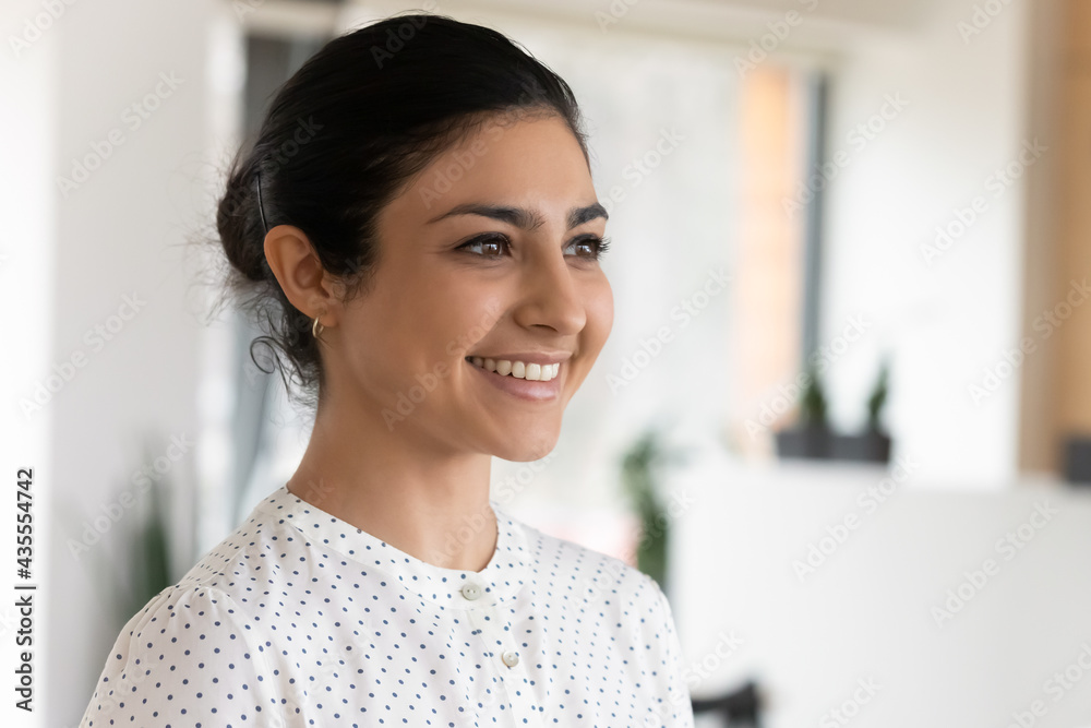Three quarter portrait of smiling confident attractive Indian businesswoman standing in office, successful young woman entrepreneur employee executive looking to aside, business vision concept Three quarter portrait of smiling confident attractive Indian businesswoman standing in office, successful young woman entrepreneur employee executive looking to aside, business vision concept