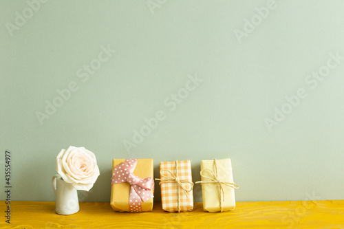 Yellow gift boxes and vase of white rose flower on wooden table. khaki green background