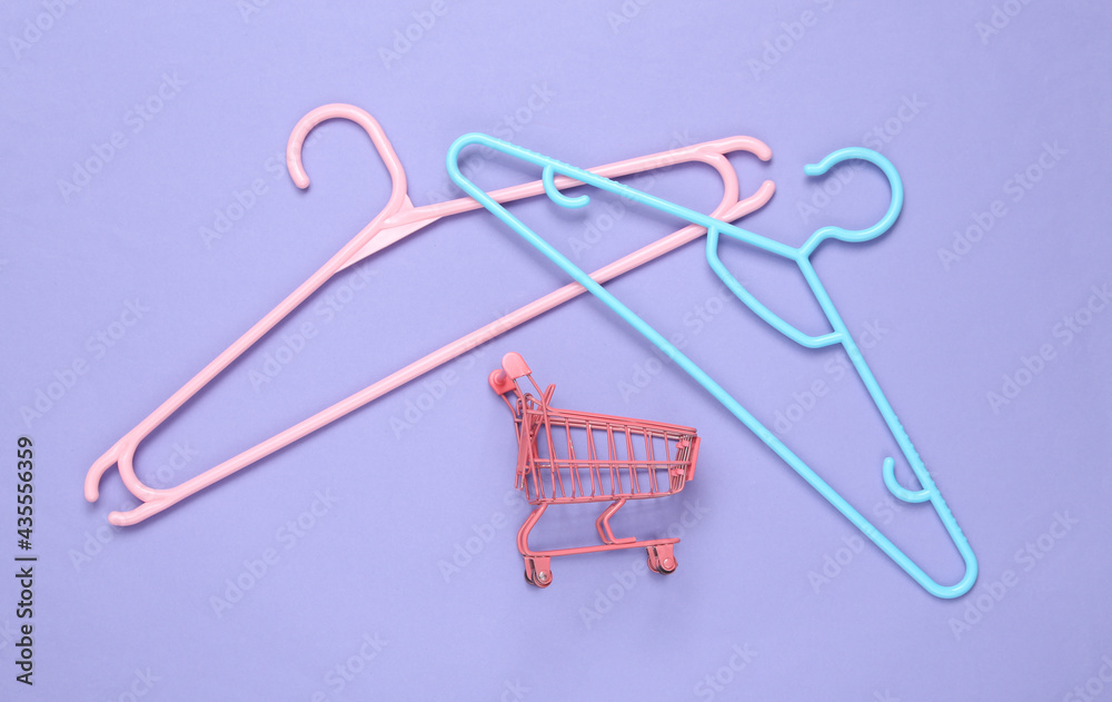 Fototapeta premium Plastic hanger with mini shopping trolley on purple background. Fashion layout. Flat lay. Top view