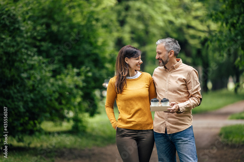 Adult man, holding cups of coffee, looking at his wife.