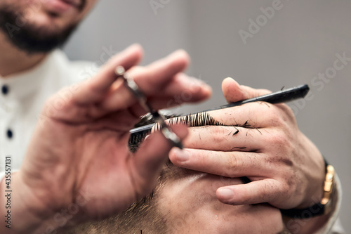 Professional barber making haircut to young man using scissors and comb at barbershop. Close-up  selective focus