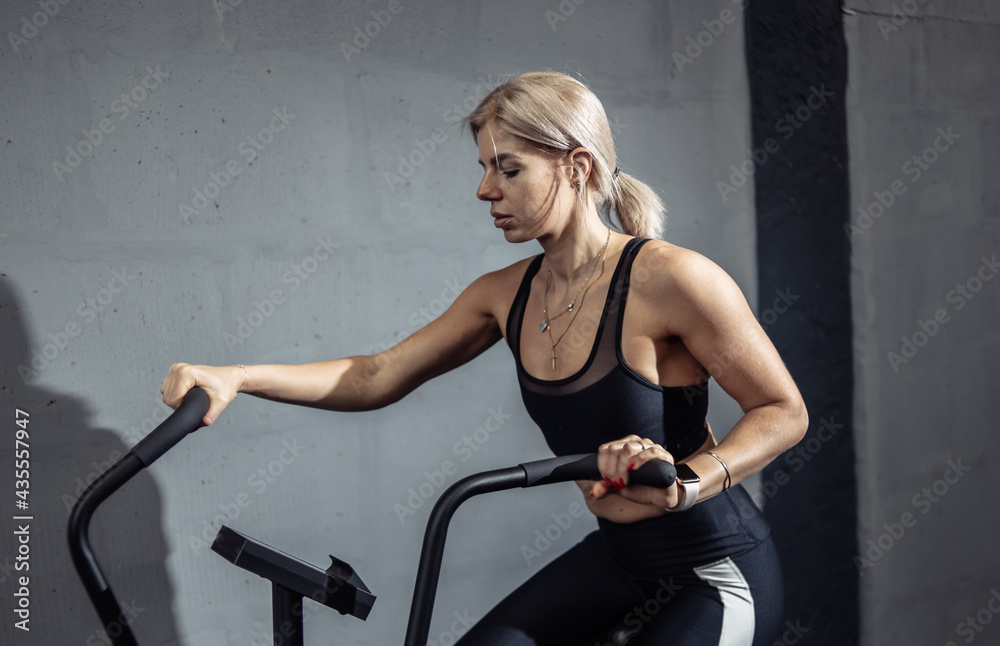 Woman doing intense cardio training on exercise bike. Fitness female using air bike for cardio workout at gym