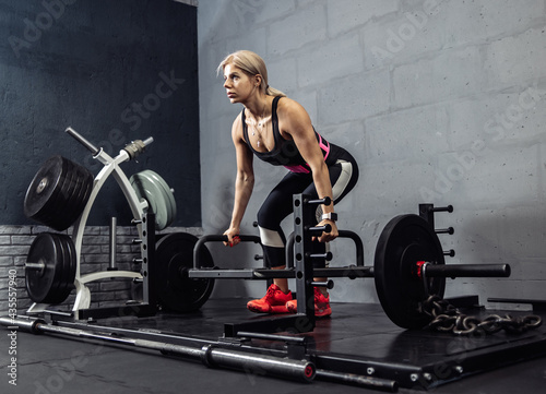 Woman exercising with heavy weights in gym. Fit female doing deadlift workout with barbell