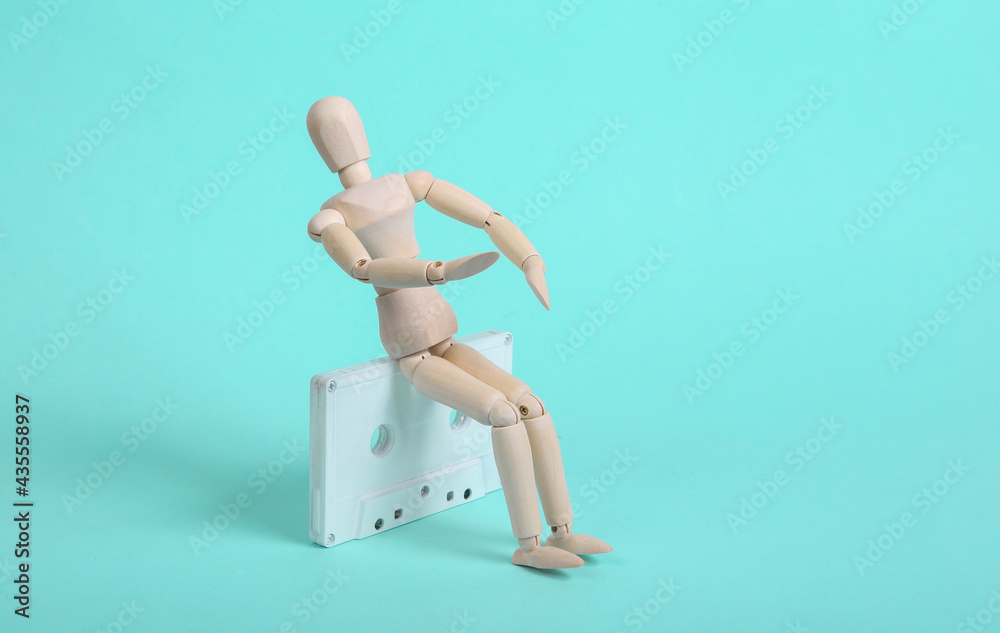 Wooden puppet with white audio cassette on blue background