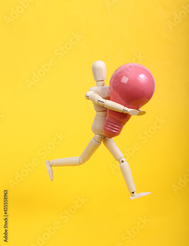 Fototapeta Wooden puppet holding pink light bulb on yellow background