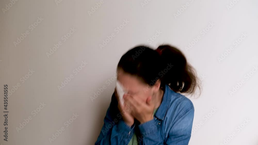 Colds, coughs, and headaches. Young Caucasian European woman on white background coughs into her hand and then blows her nose into white paper napkin. Sick girl is feeling pain. 4K footage. Colds, coughs, and headaches. Young Caucasian European woman on white background coughs into her hand and then blows her nose into white paper napkin. Sick girl is feeling pain. 4K footage.